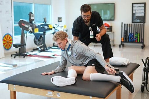 Ryan Lasko, a minor league prospect with the Athletics who was paralyzed in an outfield collision moves onto a mat table as Physical Therapist Daniel Gabrielli looks on at the Kessler Institute for Rehabilitation in West Orange, N.J., Tuesday, Sept. 15, 2026. (AP Photo/Matt Rourke) (AP Photo/Matt Rourke)