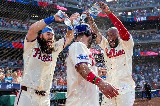 Brandon Marsh, izquierda, de los Filis de Filadelfia, junto con Bryan De La Cruz, derecha, bañan a Kyle Schwarber, centro, después de la victoria en el partido de béisbol de Grandes Ligas contra los Cardenales de San Luis, el domingo 23 de agosto de 2026, en Filadelfia. (AP Foto/Laurence Kesterson) (AP Photo/Laurence Kesterson)