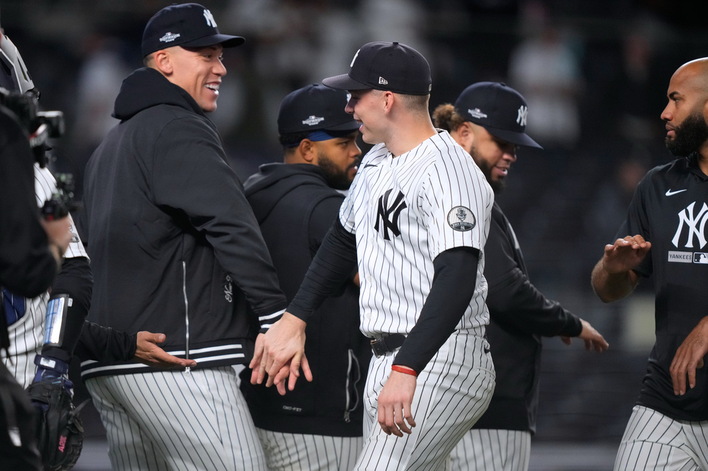 Aaron Judge, in a team jacket rather than a uniform, smiles with Ben Rice in pinstripes as the Yankees celebrate beating Boston in the Wild Card Series.