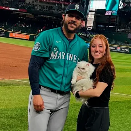 Seattle Mariners pitcher Andrés Muñoz stands on the field with his wife Wendy Almodóvar holding their cat Matilda after a home game.