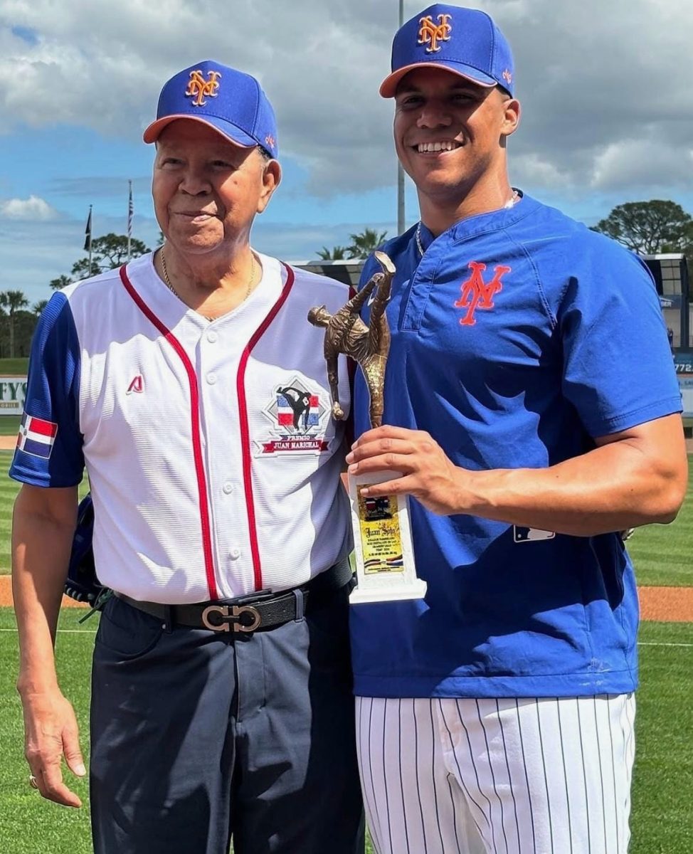 Juan Soto, wearing a Mets uniform, holds the Juan Marichal Award while standing beside the legendary Dominican pitcher on the field.