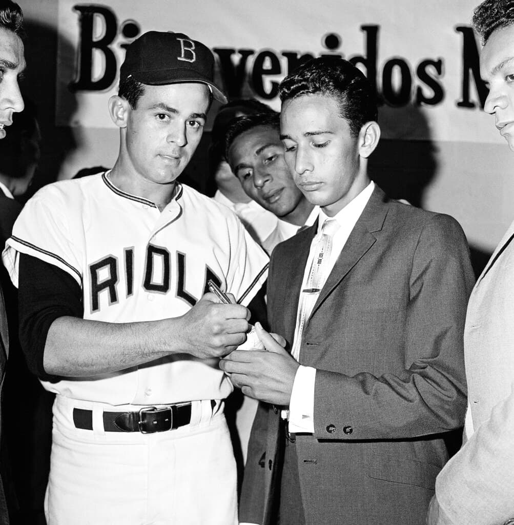 Title: Baltimore Oriole Luis Aparicio Image ID: 630518063 Article: Alfredo Hernandez, right, a member of the Venezuelan All-Star Baseball Team, gets an autograph from Baltimore Oriole shortstop Luis Aparicio, also from Venezuela, May 18, 1963. The all stars were in Baltimore to watch the series between the Orioles and the White Sox. (AP Photo/Jim Bourdier)