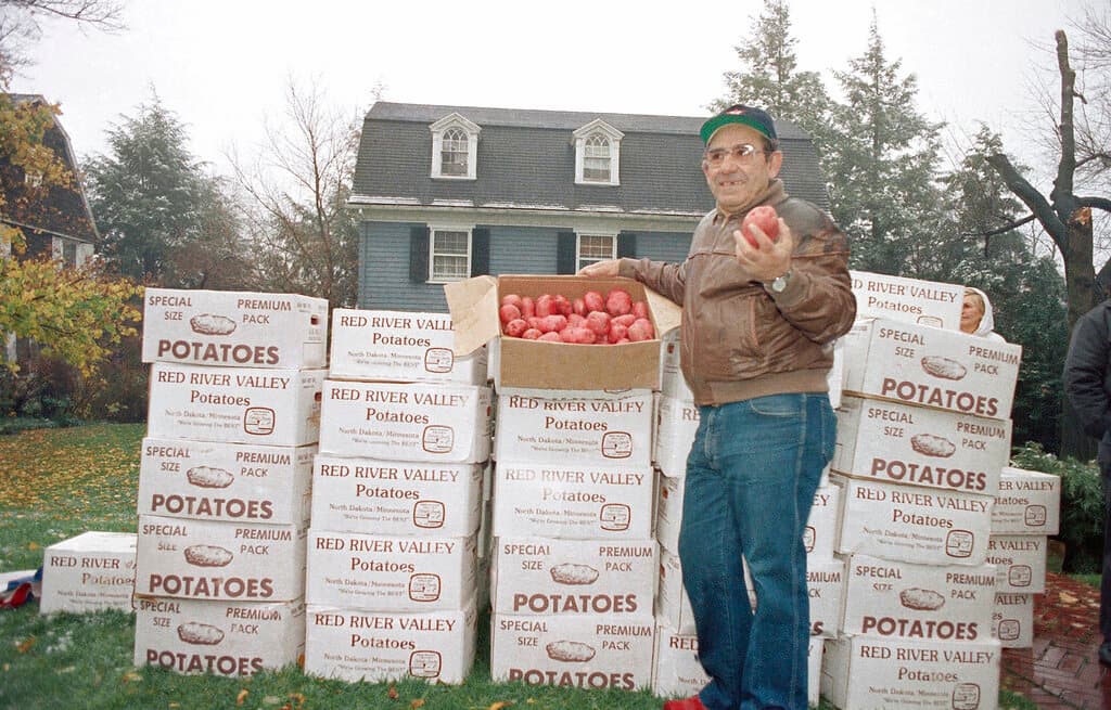 Title: Berra And Potatoes 1985 Image ID: 8511260112 Article: Yogi Berra stands in front of his home in Montclair, N.J. with 23 tons of potatoes delivered from North Dakota, Nov. 26, 1985. Berra had made a bet that North Dakota couldn't produce enough potatoes to fill his front yard, and they proved him wrong. The potatoes will be distributed to hundreds of needy New Yorkers for Thanksgiving. (AP Photo)