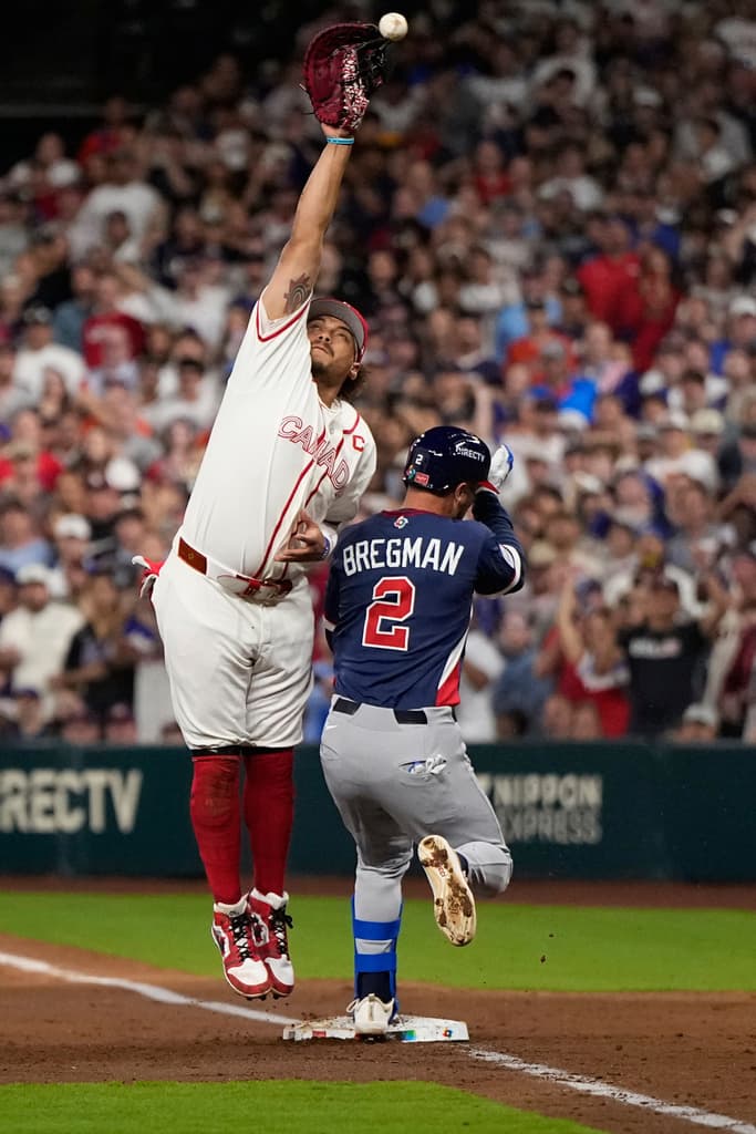 Alex Bregman (2) is safe at first base as Canada first baseman Josh Naylor, left, reaches for a wild throw during the third inning of a World Baseball Classic quarterfinal game, Friday, March 13, 2026, in Houston. (AP Photo/David J. Phillip)